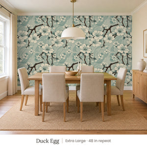 Sakura Duck Egg peel and stick wallpaper, extra large 48 in repeat, in a dining room with a wood table and upholstered chairs